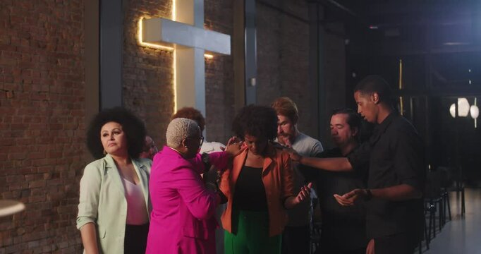 Prayer group supporting a woman in a spiritual moment of faith and connection, hands placed on her shoulders as others share blessings and unity under a cross