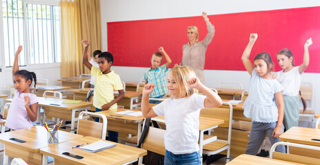 Cheerful preteen pupils doing little warm-up in class with female teacher at lesson in elementary...