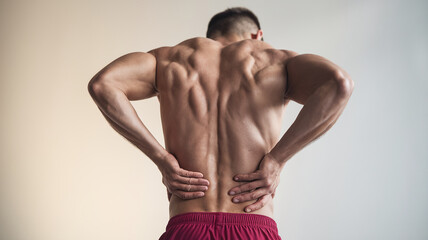 Fototapeta premium Rear view of muscular male torso, hands on lower back, suggesting back pain or discomfort. Image showcases physical health, fitness, and potential injury