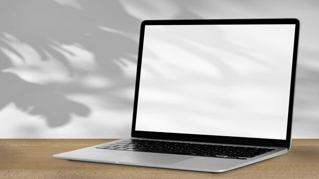  laptop stands on a wooden table with a white background behind it, a shadow falls on it, which sways gently in the wind.