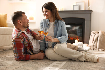 Happy couple with glasses of wine near fireplace on floor at home