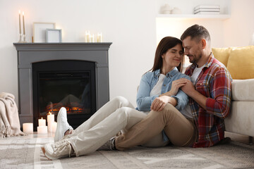 Fototapeta premium Cute couple sitting near fireplace on floor at home