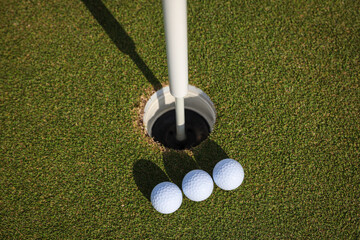 Three golf balls near hole on green field, Close-up top view of three white golf balls resting beside.