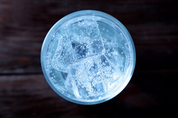 Refreshing soda water with ice cubes in glass on wooden table, top view