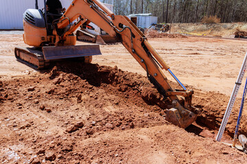 Construction worker uses an excavator to dig trench in dirt field during works construction