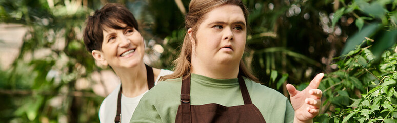 Mature woman guides her young colleague with Down syndrome in a vibrant greenhouse setting