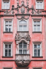 Fototapeta premium Ornate architectural features on a pink building facade showcasing intricate designs and window details in a charming urban setting