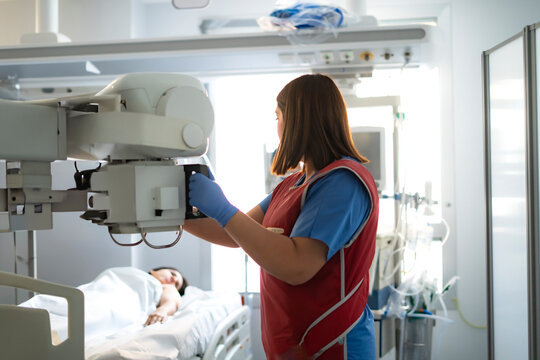 Radiologist positioning x-ray machine over patient lying in hospital bed
