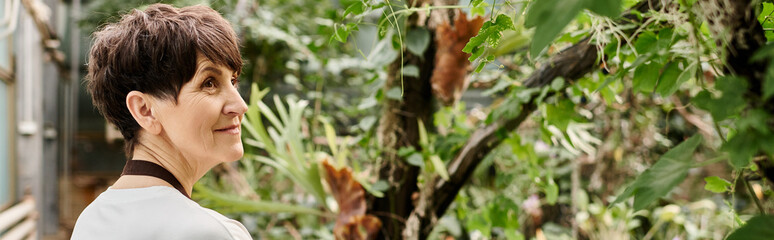 Mature woman tending to lush greenery in a vibrant greenhouse, exuding confidence and grace