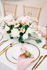 Small pomegranate lies on a pink knotted napkin in a plate on a set table