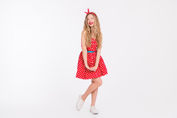 Stylish young woman posing in retro red polka dot dress with playful expression on white background