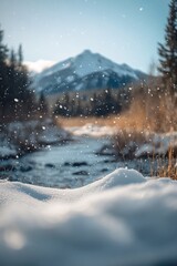 Fototapeta premium Snow falling over a calm stream with a mountain in the background.