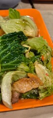 Stir-fried morning glory and crispy pork on an orange plate