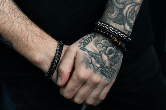  Tattooed hands in a close-up view, featuring detailed ink of a bird and adorned with stylish leather bracelets. The image highlights personal expression through body art and accessories