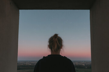 Fototapeta premium A woman with a ponytail is looking out of a window at the sky
