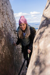 Fototapeta premium Young woman hiker descending through a narrow passage between rocks using a rope