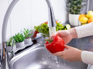 Woman hands washing a red bell pepper to prepare a fresh salad in the kitchen