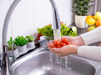 Woman hands washing fresh cherry tomatoes to prepare a fresh salad
