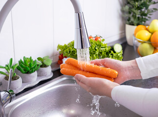 Woman hands washing fresh carrots in the kitchen