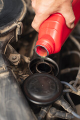 Close-up of a man's hand pouring a red container of motor oil into a car engine