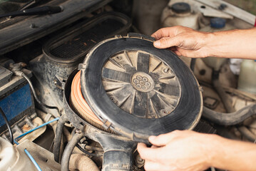 Close-up of a man&rsquo;s hands installing or removing a round air filter cover inside a car engine
