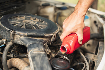 Close-up of a man's hand pouring a red container of motor oil into a car engine