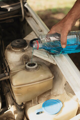 Close-up of a man's hand pouring blue antifreeze fluid from a plastic bottle into the reservoir 