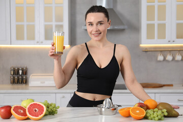 Woman in fitness clothes with glass of juice at white marble table indoors