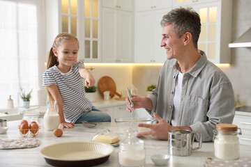 Father and his daughter making dough at white marble table in kitchen