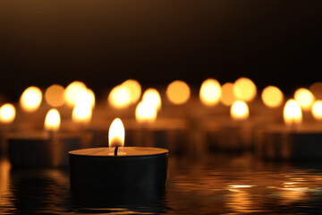 Candles burning on surface covered with water in darkness