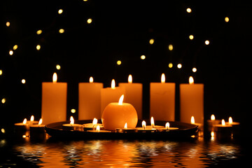 Candles burning on surface covered with water in darkness