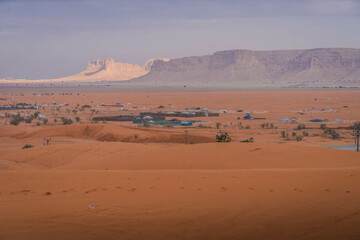 Wide view of a remote desert village in the Arabian Peninsula, Saudi Arabia, nestled among sand and beautiful rock formations.
