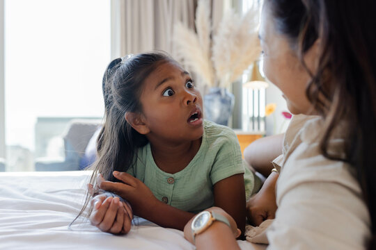 Shocked surprised young daughter looking up at mother at home in bedroom