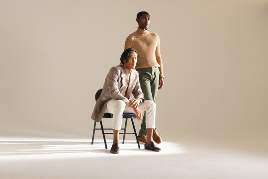 African american man sitting on chair in minimalist studio with asian man standing