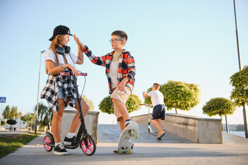 Cute kids in stylish casual clothes in skate park. They ride on skates and scooters. Summer vacation