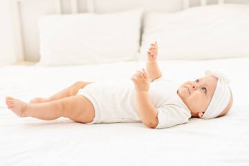 cute little baby on a white bed at home in a bodysuit lying on the back and smiling, newborn baby top view.
