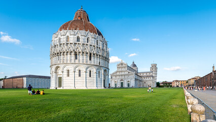 Scenic view of Piazza dei Miracoli in Pisa, Italy, with the Leaning Tower, Baptistery, and Cathedral. The green lawn contrasts with the white marble architecture of this UNESCO site.