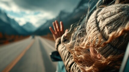 10. Hand reaching out of a car window catching wind on a road trip with mountains ahead 