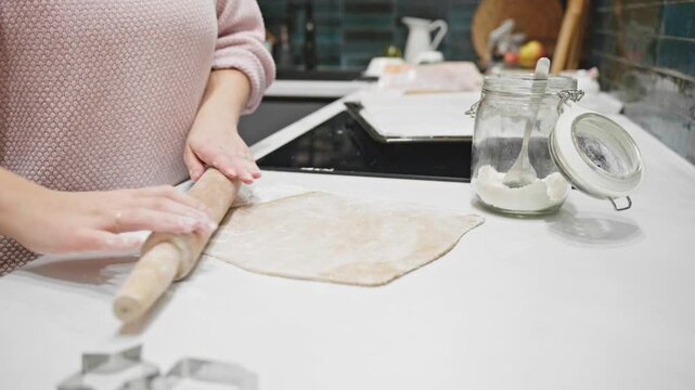 Hands work to roll gingerbread dough on a white surface, with flour and cookie cutters nearby. A delightful moment of festive preparation for holiday treats