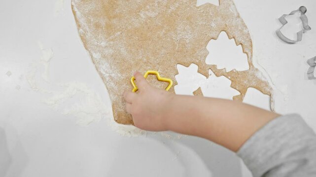 A kid assists in cutting gingerbread dough into festive shapes with cookie cutters. The scene reflects the joy of family traditions and holiday baking fun