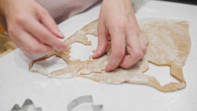 Holiday baking in progress as hands cut festive shapes from gingerbread dough with cookie cutters. A cozy and creative moment filled with seasonal charm. Toddler helps to make cookies.
