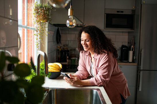 Smiling woman using smartphone next to sink in modern kitchen