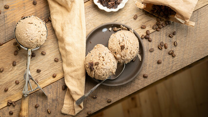 Scoops of gourmet coffee flavored homemade ice cream on wooden table with coffee beans spilling out of bag.