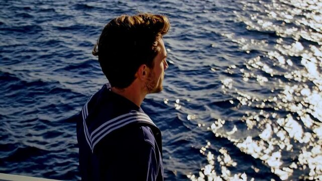 Sailor is standing on ship. Sailor is wearing naval uniform. Ocean is calm and sky is clear.