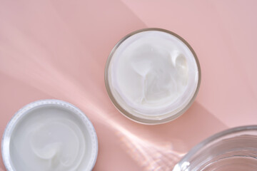 An open jar of cream with its texture on a pink background.