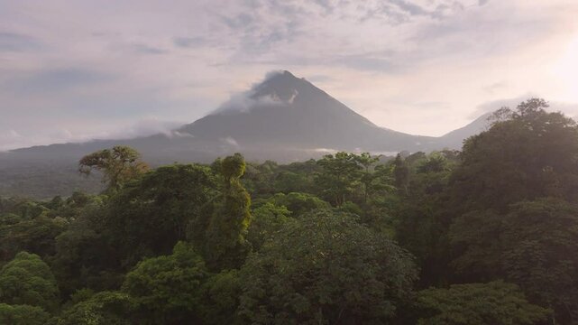 Experience the breathtaking aerial view of Arenal Volcano and serene Laguna de Arenal at sunrise, showcasing lush forests and the enchanting misty atmosphere of beautiful Costa Rica