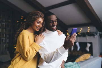 Smiling couple enjoys online shopping on a smartphone, standing close together in a cozy, festively decorated home. They share excitement and connection, embodying joy of modern digital convenience