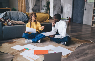 Engaged couple sitting on the floor discussing documents, collaborating on finances or work...