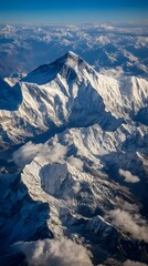 Obraz premium Majestic Peaks: A breathtaking aerial perspective unveils a towering mountain range, their peaks draped in pristine snow and ice, set against a vast expanse of blue sky.