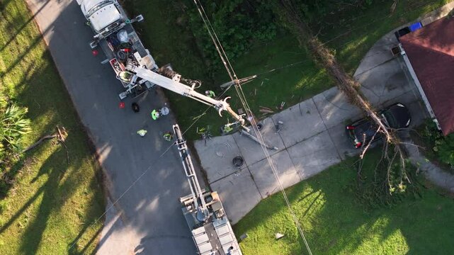 Electrician workers repairing damaged power lines using bucket trucks after hurricane in Florida residential area.
